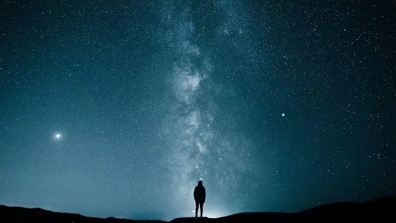 A silhouette facing the Milky Way rising above a dark ridge.
