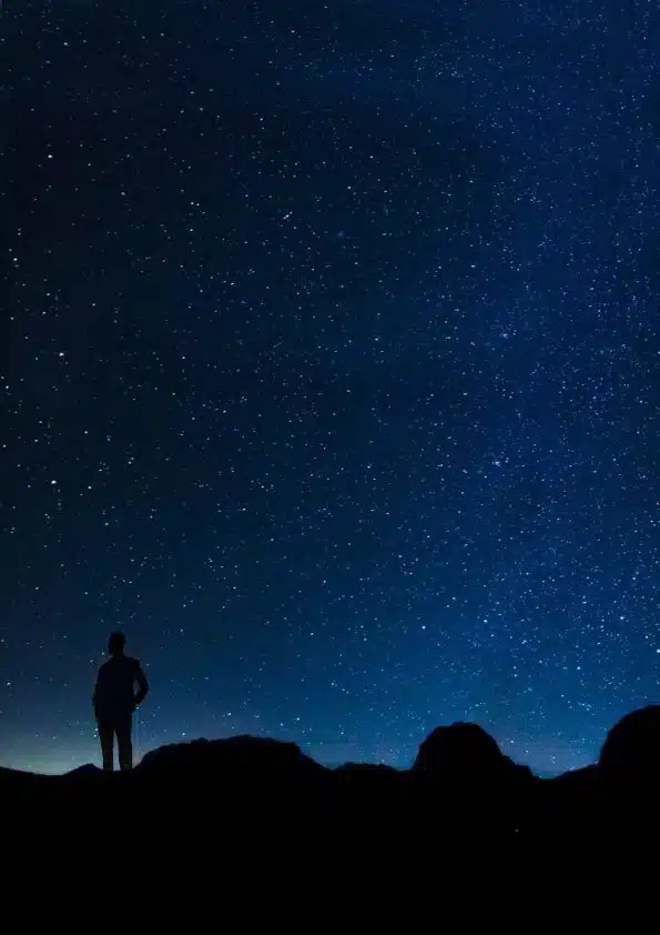A person standing among rocks beneath a deep blue field of stars.