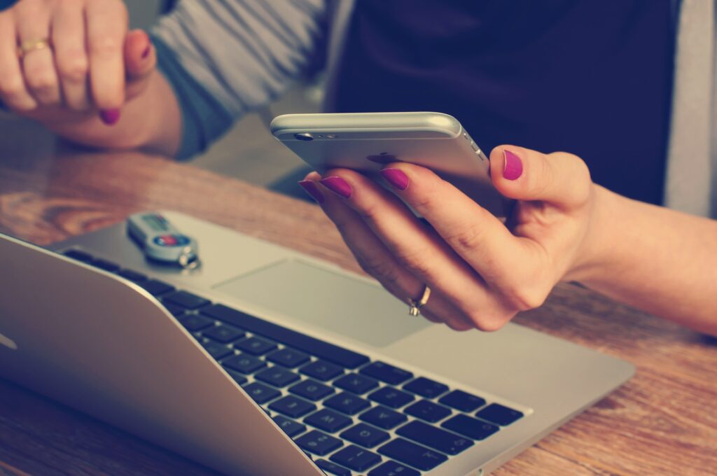Hands scrolling a phone beside an open laptop, the everyday shape of screen addiction
