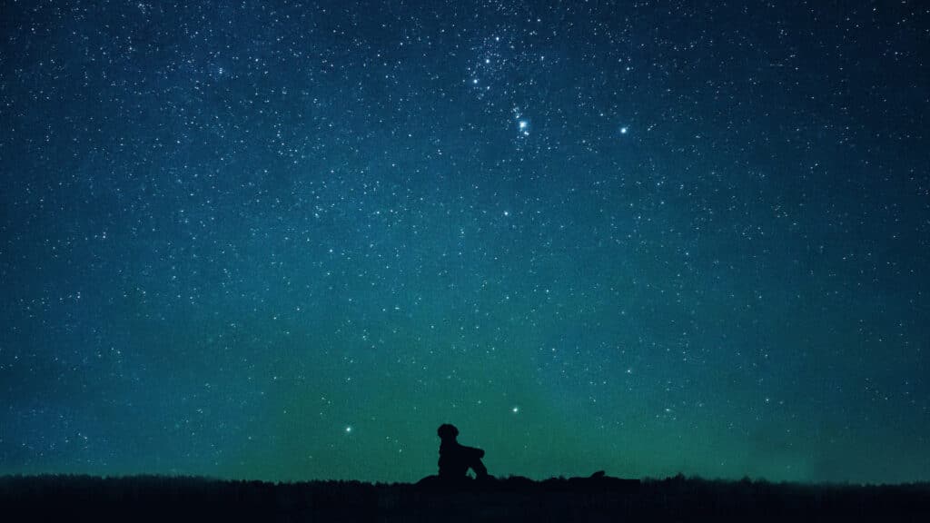 Shadow figure sitting under a starry sky