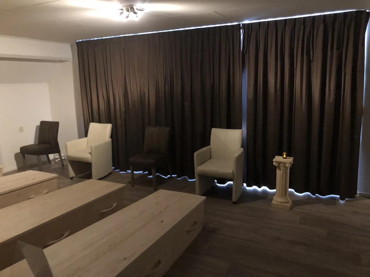 A memento mori coffin seminar room in the Netherlands: empty chairs facing three closed pine coffins, with one candle on a pillar